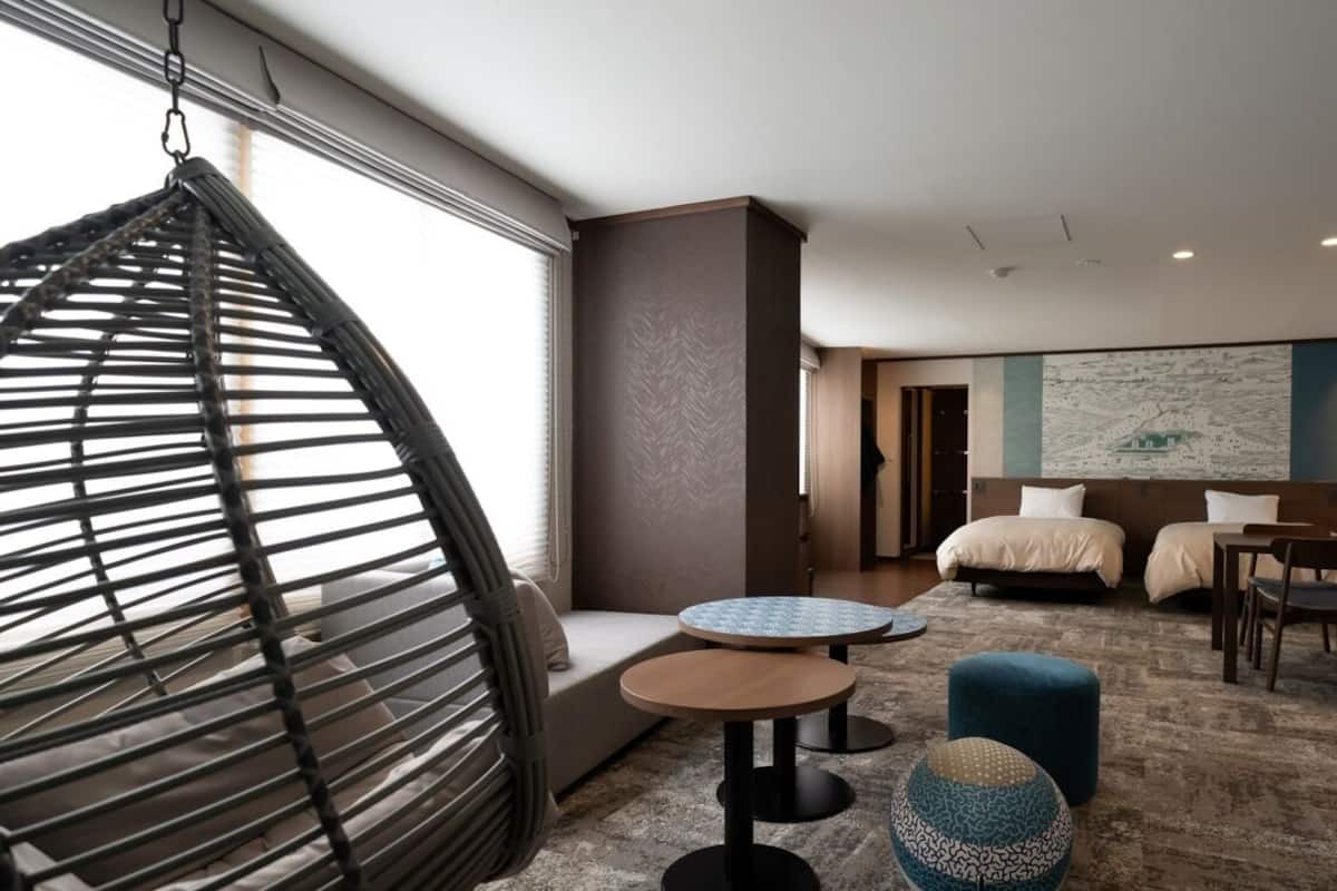 A hotel room with a bed, two round tables, a hanging chair, and a large abstract painting on the wall.