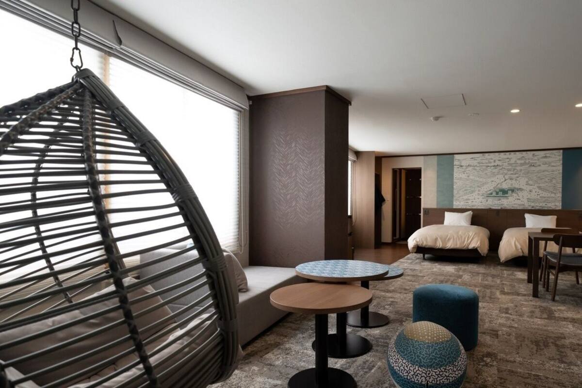 A hotel room with a bed, two round tables, a hanging chair, and a large abstract painting on the wall.