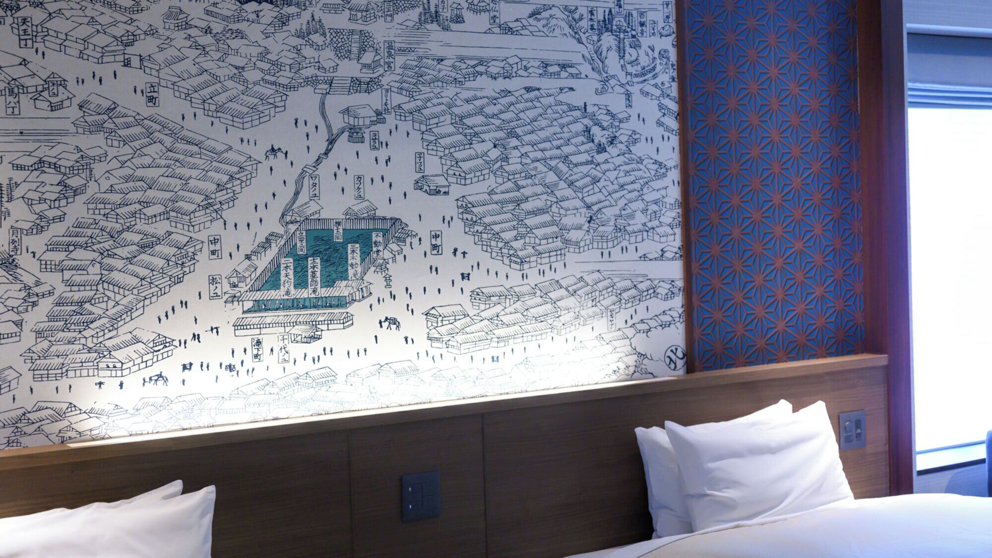 A hotel room with a large wall mural depicting a traditional town scene, a bed with white linens, and a patterned curtain.