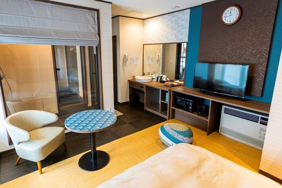 A modern hotel room with a bed, a round table, a chair, a TV, a mirror, and a heater.