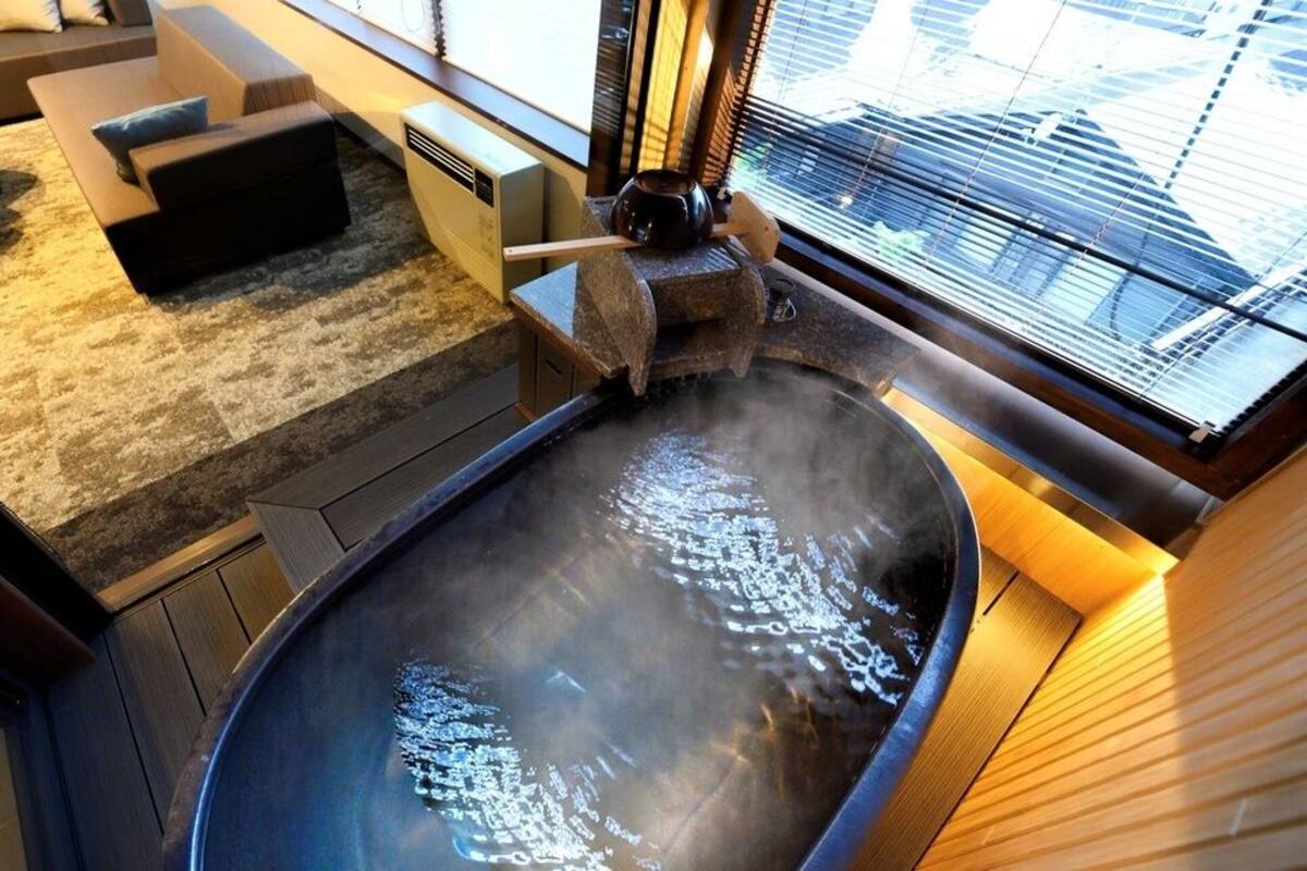 A hot tub with steam, a sofa, a small table, and a window with blinds.