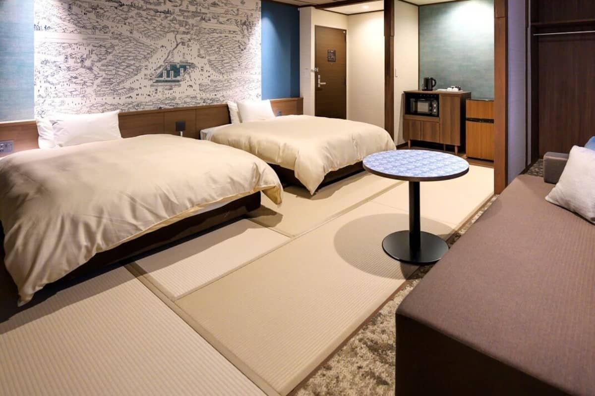 A hotel room with two beds, a sofa, a small round table, a microwave, and a television.