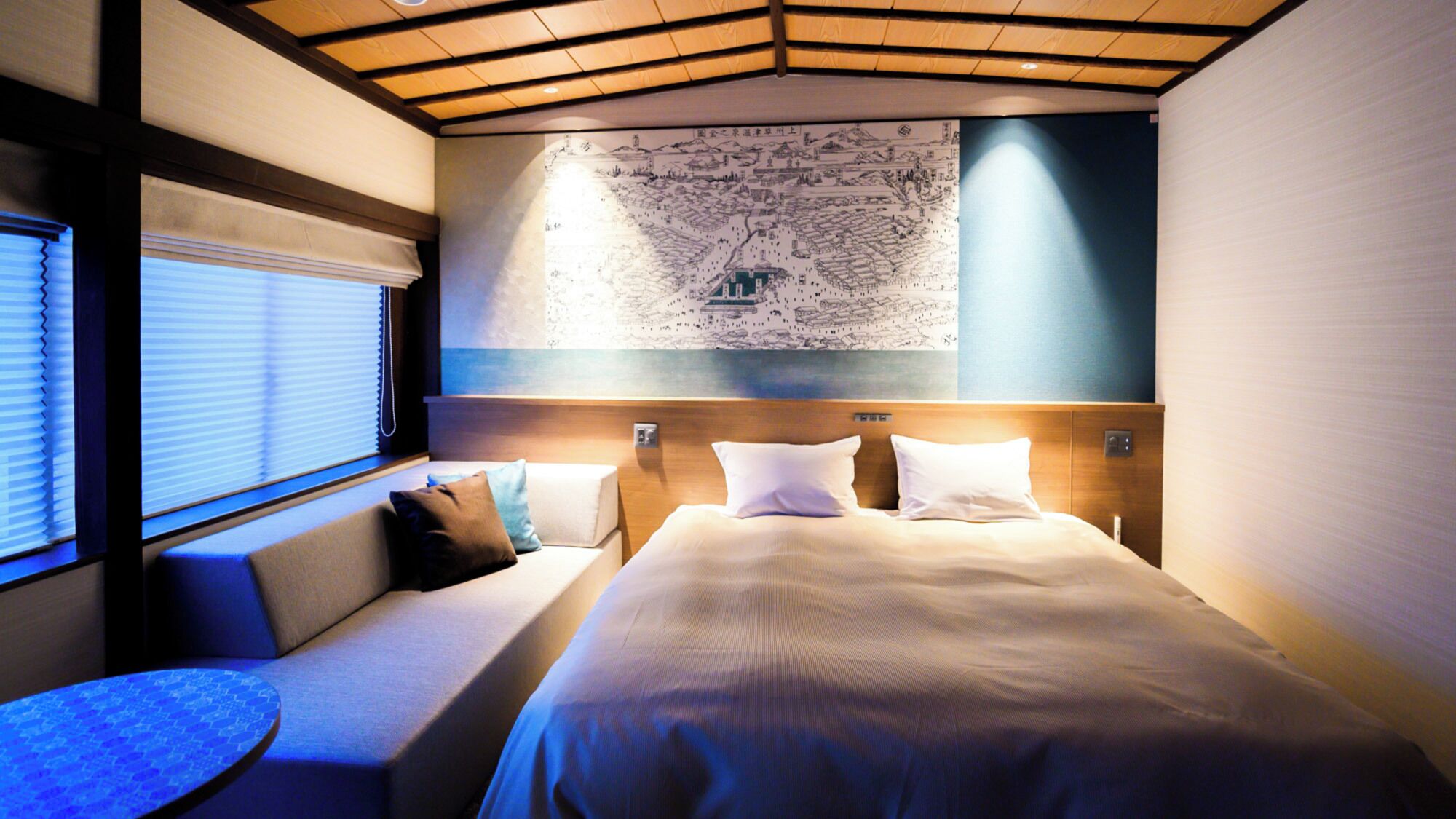A hotel room with a large bed, a seating area with cushions, a map on the wall, and a window with blinds.