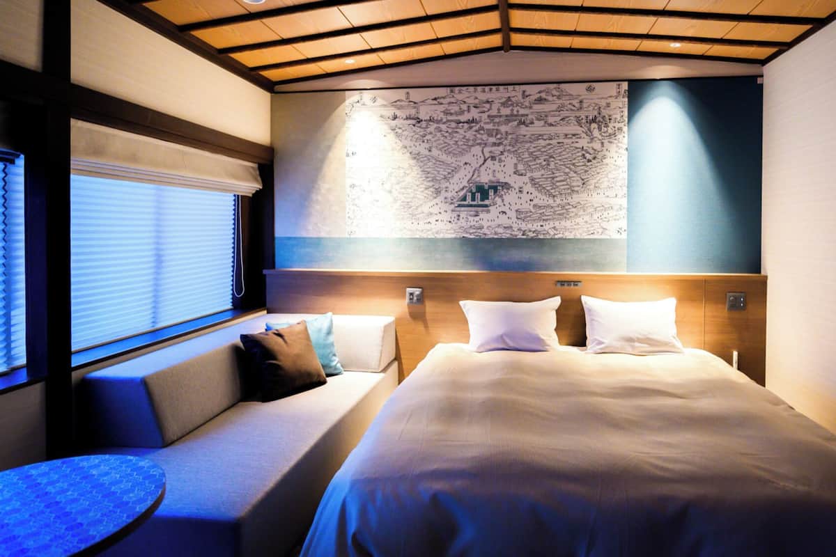A hotel room with a large bed, a seating area with cushions, a map on the wall, and a window with blinds.