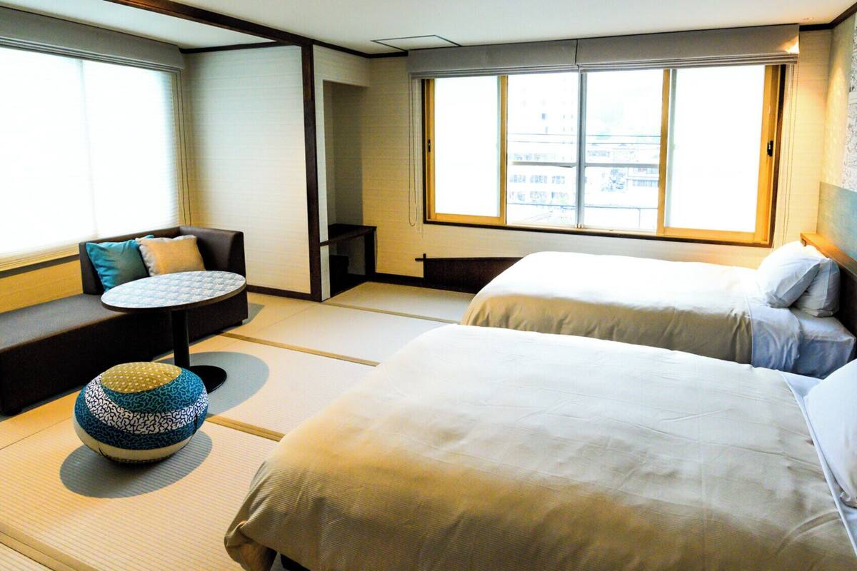 A hotel room with two beds, a sofa, a small table, and a tatami mat.
