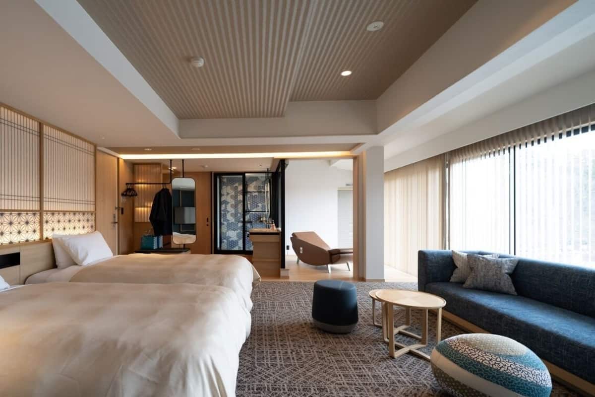 A hotel room with a large bed, a sofa, a small table, and a decorative screen.