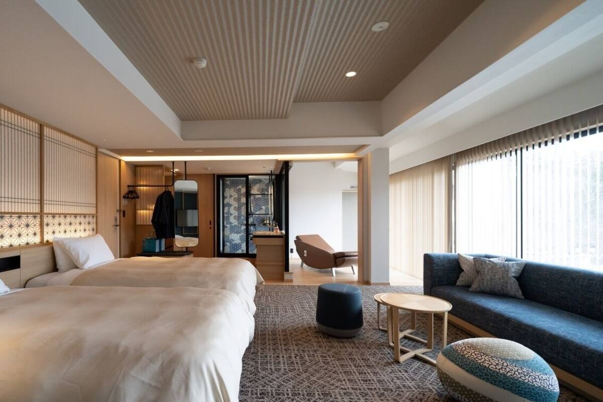 A hotel room with a large bed, a sofa, a small table, and a decorative screen.
