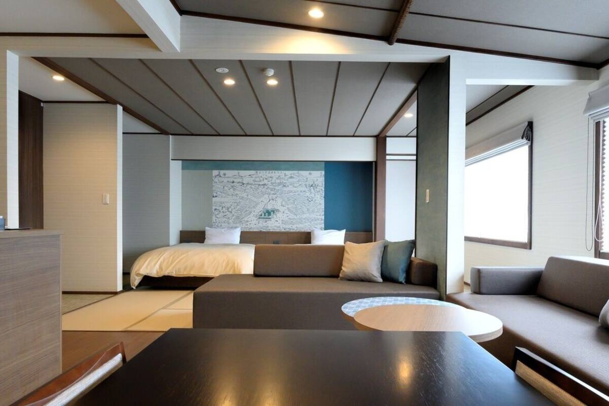 A modern hotel room with a bed, seating area, and a large window.