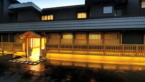 Un edificio japonés tradicional con techo de tejas, una puerta de entrada de madera y una superficie acuática reflectante en primer plano.