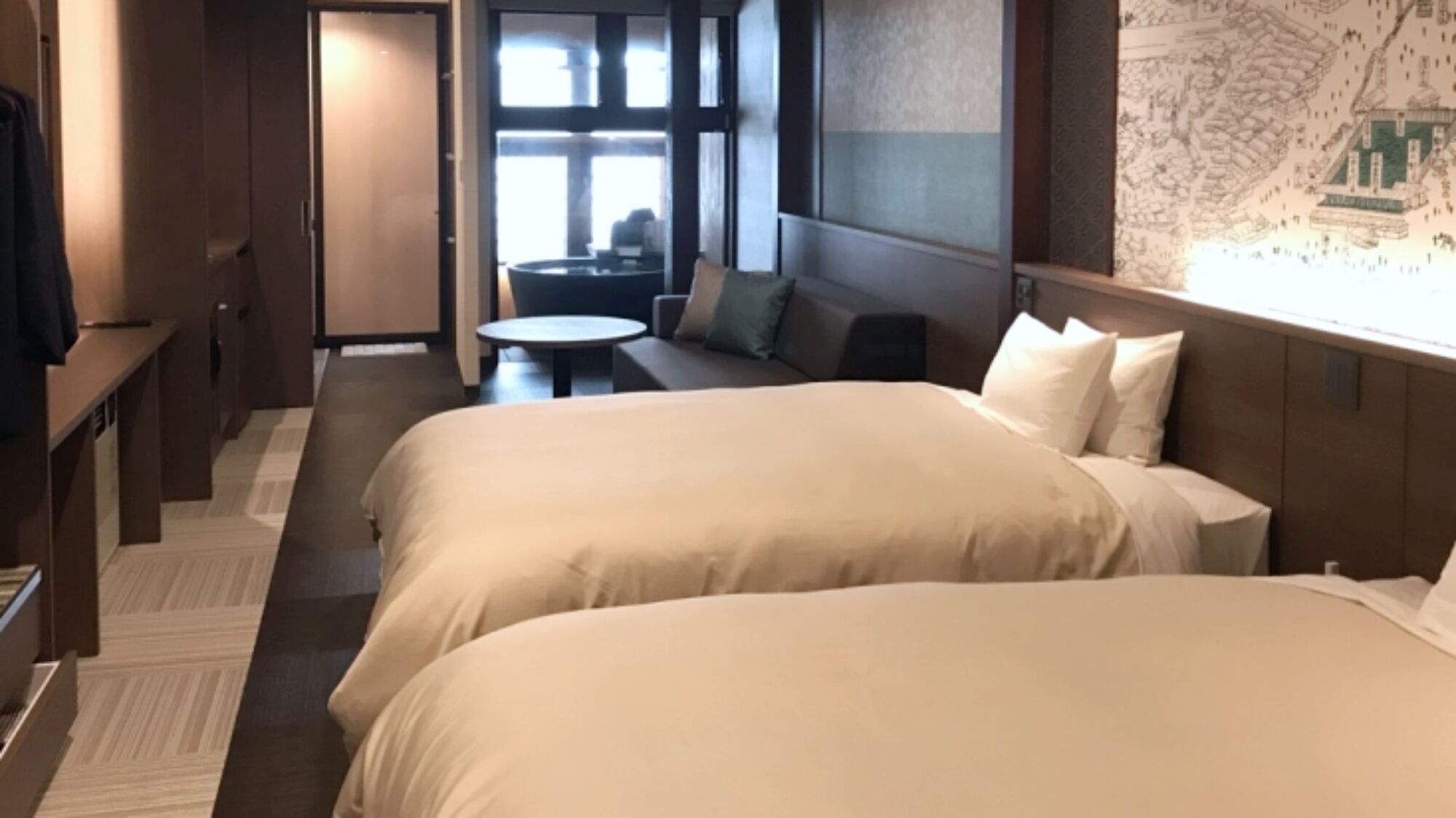 A hotel room with two beds, a sofa, a small table, and a map on the wall.