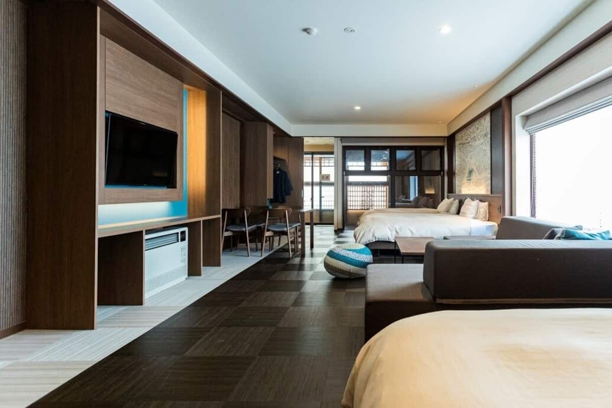 A hotel room with a large bed, a sofa, a TV, and a desk with chairs.