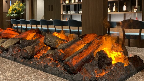Zona de bar con una chimenea central, asientos y estantes llenos de botellas.