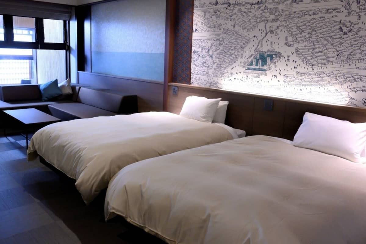 A hotel room with two beds, a sofa, a desk, and a large window.
