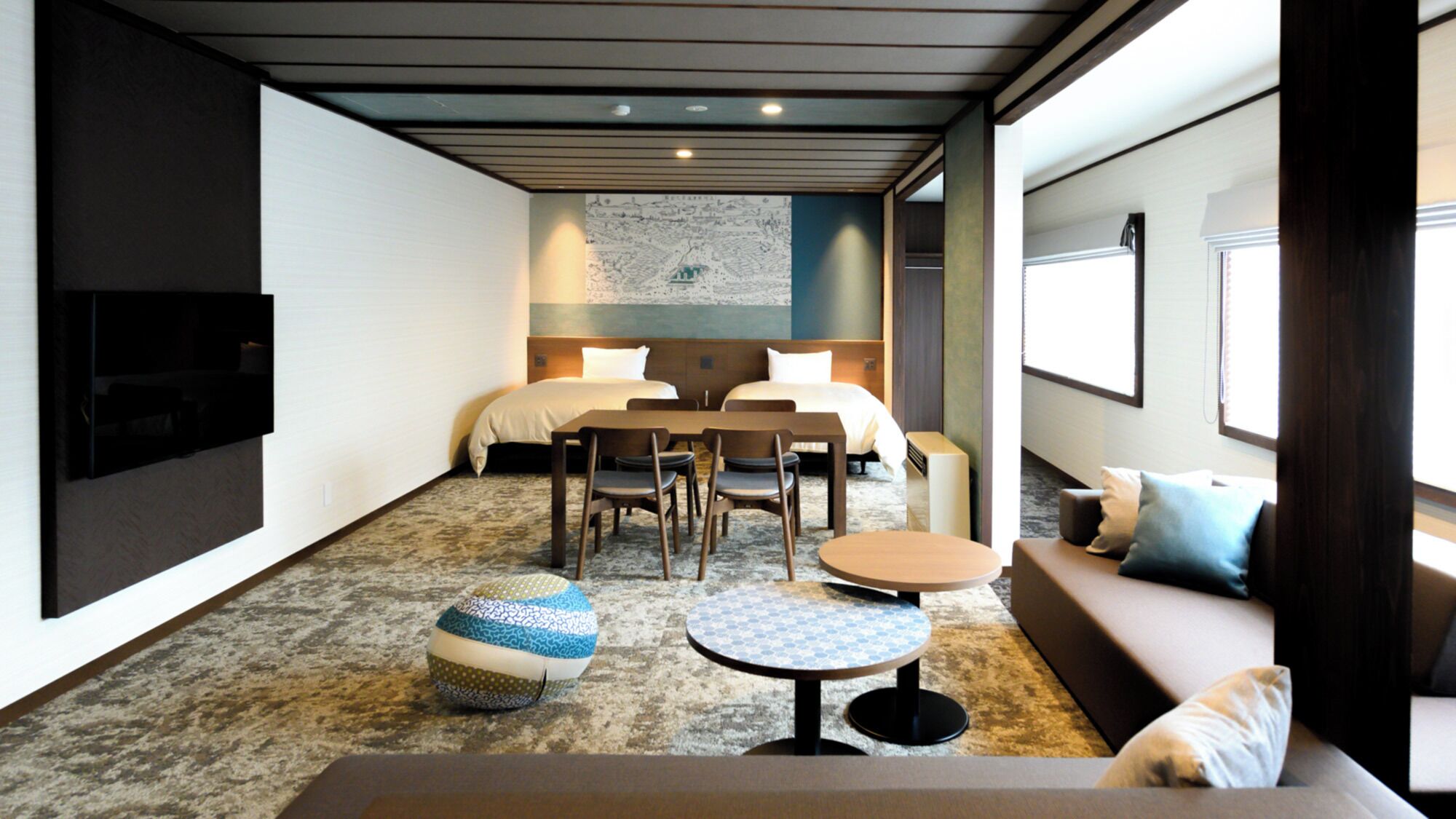 A hotel room with a bed, two bedside tables, a sofa, a TV, a map on the wall, and a carpeted floor.