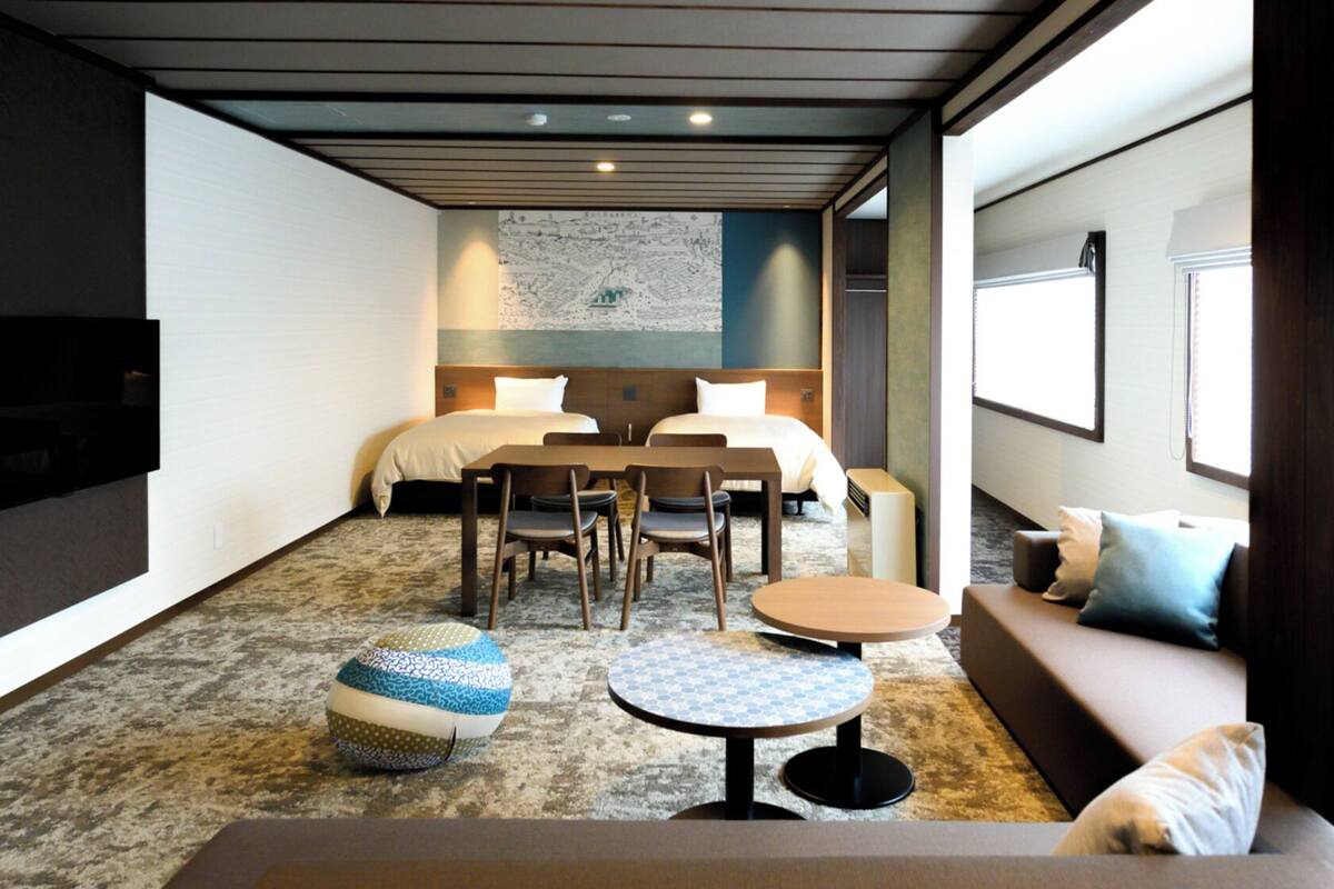 A hotel room with a bed, two bedside tables, a sofa, a TV, a map on the wall, and a carpeted floor.