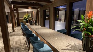 Una larga mesa de conferencias con sillas azules, pilares de madera y una alfombra estampada.