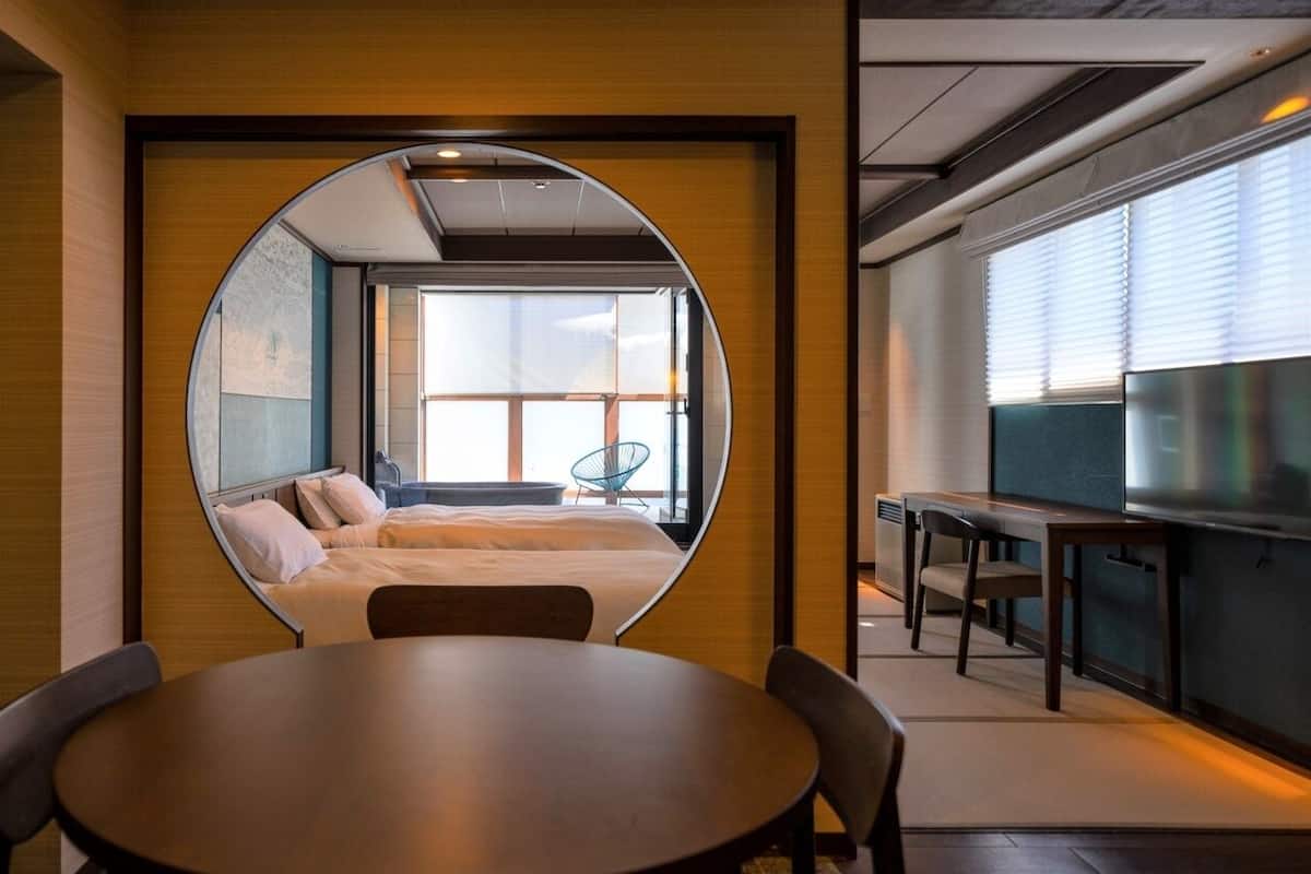 A hotel room with a round mirror reflecting a bed, a dining table, and a TV.
