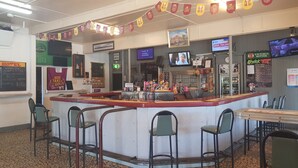 A restaurant with a counter, bar stools, and a TV screen. - Kerwick Hotel (Redbank)