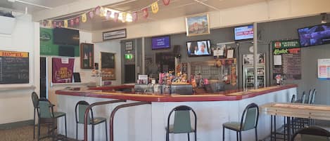 A restaurant with a counter, bar stools, and a TV screen.