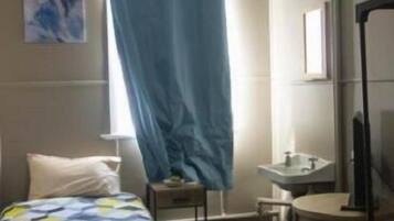 A hotel room with a bed, a small table, a chair, a TV, and a window with a curtain.
