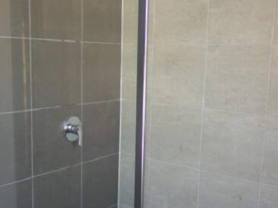 A glass-enclosed shower area with tiled walls and a metal showerhead.