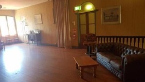 A spacious room with a wooden floor, a leather sofa, a small table, and a chair. There is a door with a green exit sign, a framed picture on the wall, and a window with curtains. - Kerwick Hotel (Redbank)