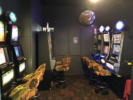 Una habitación con máquinas tragamonedas, taburetes de bar y un espejo en la pared.