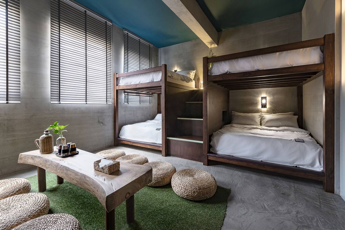 A compact room with bunk beds, a wooden table with a plant, and woven poufs.