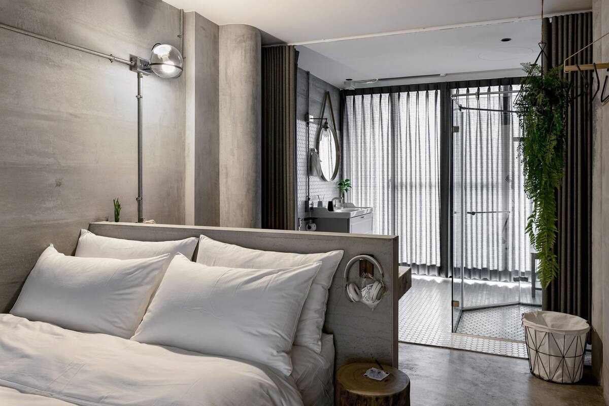A modern bedroom with a large bed, a bedside table, a lamp, and a view of a balcony.