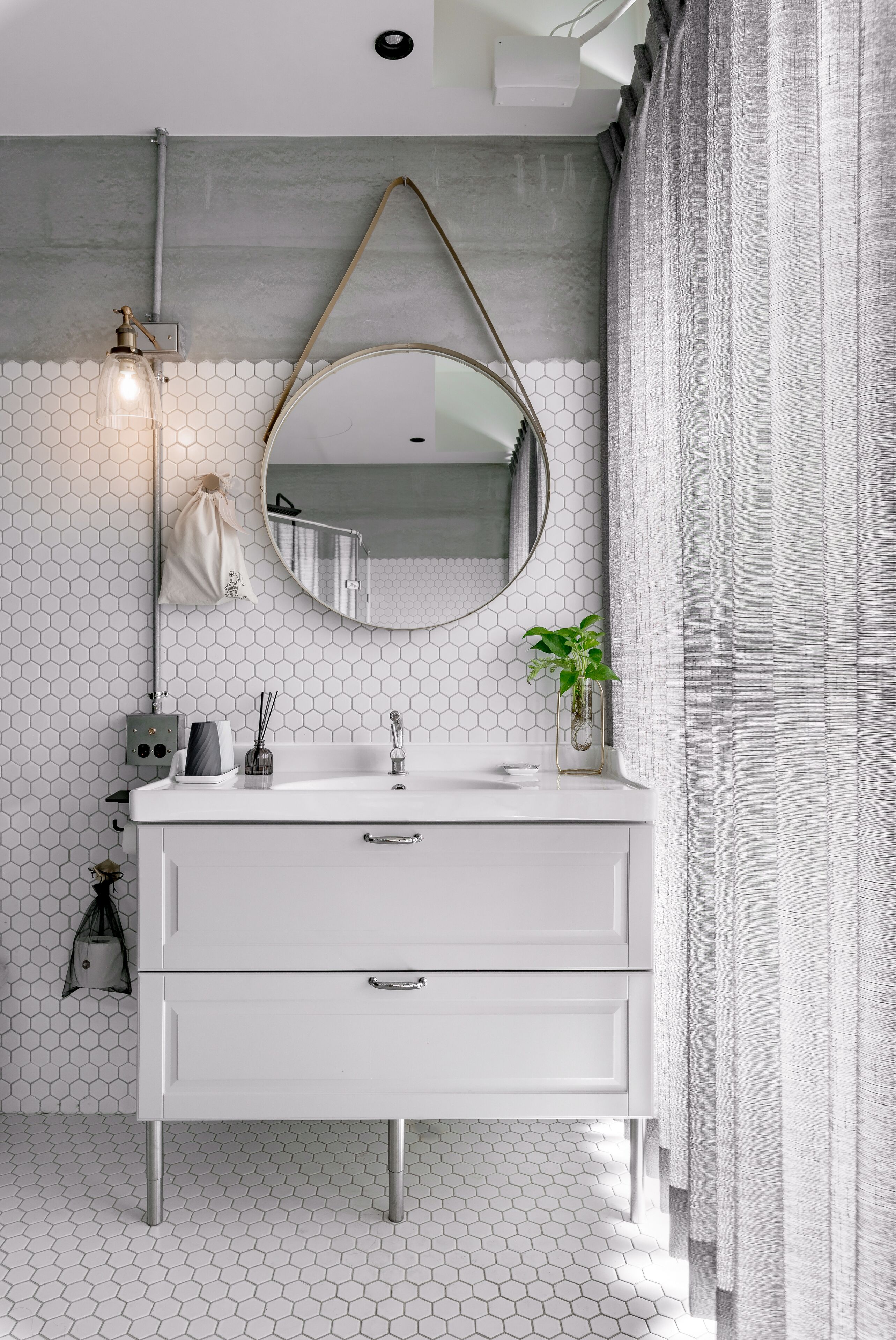 Une salle de bain moderne avec un meuble-lavabo blanc, un miroir rond, un revêtement mural en carreaux hexagonaux et une plante suspendue.