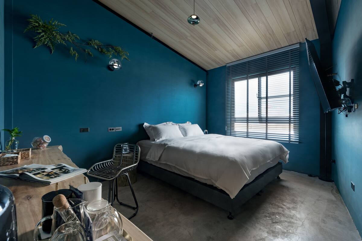 A bedroom with a bed, a desk, and a window with blinds.