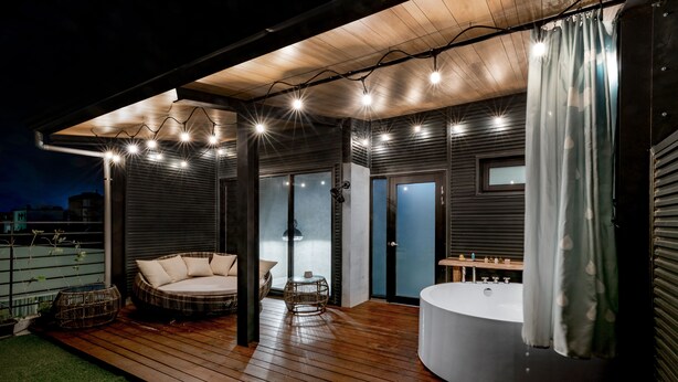 Une terrasse extérieure dotée d’un jacuzzi, d’un espace salon et d’un patio couvert agrémenté de guirlandes lumineuses.