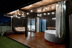 An outdoor deck with a hot tub, seating area, and a covered patio with string lights.