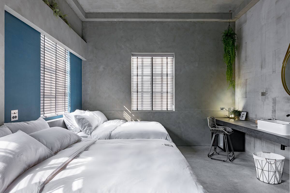 A modern bedroom with two beds, a desk, and a hanging plant.