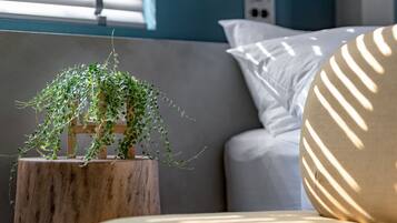 Una planta sobre un taburete de madera, una almohada blanca y un sofá con la luz del sol proyectando sombras.