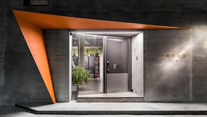 Une entrée d’hôtel moderne, dotée d’un design géométrique, d’une porte en verre et laissant entrevoir un intérieur agrémenté de plantes en pot.
