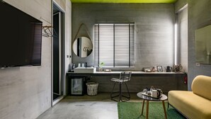 Une chambre d’hôtel de taille réduite, comprenant un lit, une petite table avec une chaise, une fenêtre avec des stores, un lavabo et un miroir.
