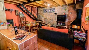 Una sala de estar acogedora con chimenea de piedra, vigas de madera, una escalera y un comedor con mesa y sillas.