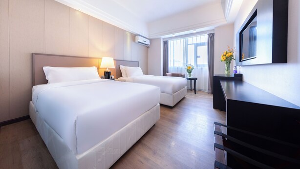 Une chambre d’hôtel avec deux lits, une télévision, un bureau et une petite table agrémentée de fleurs.