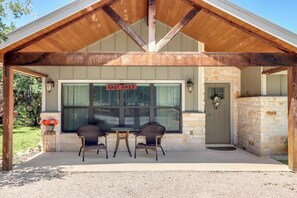 A covered patio with two wicker chairs and a table, a sign reading 'LAZY DAZE,' and a stone wall entrance.