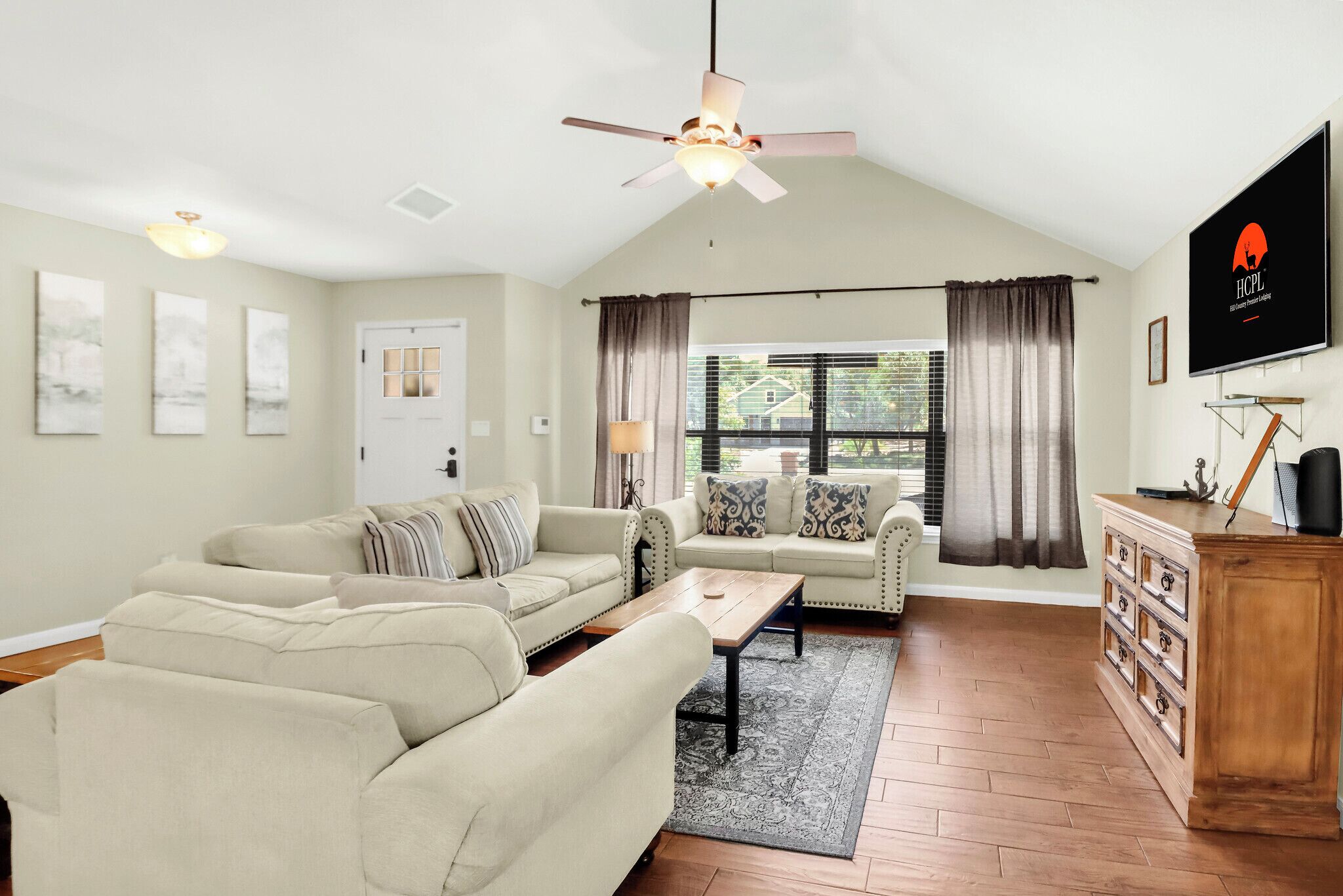 A living room with a sectional sofa, a coffee table, a TV, and a ceiling fan.