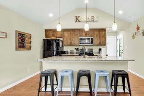 A kitchen with wooden cabinets, a stainless steel refrigerator, a microwave, and a large island with bar stools. - Charming cottage near Tubing, Whitewater, Boat Ramps and more!!!! (Canyon Lake)