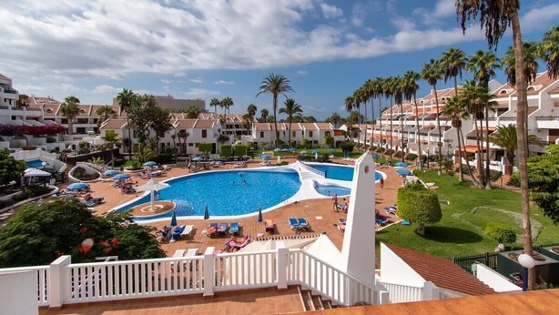 Ein Resort mit einem zentral gelegenen Swimmingpool, umgeben von Liegebereichen und Palmen.