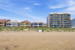 A beachfront hotel with multiple buildings, a sandy beach in the foreground, and a clear sky.