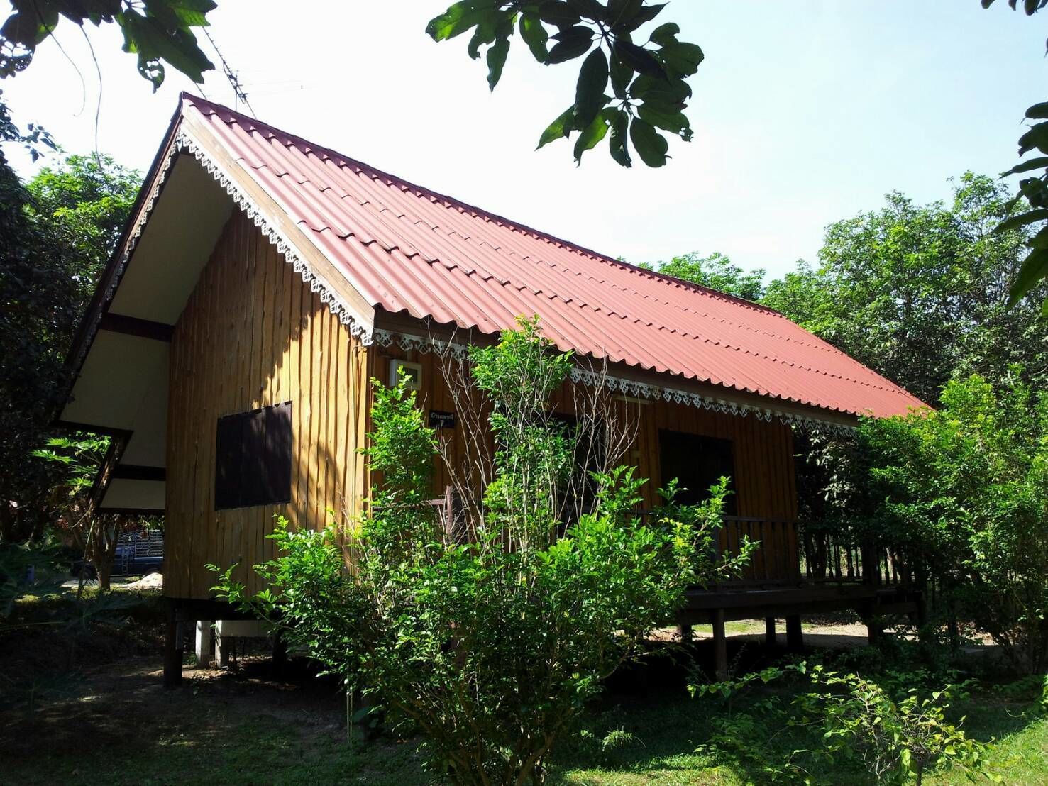 A wooden cabin with a red roof, surrounded by greenery.