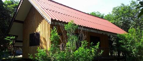 A wooden cabin with a red roof, surrounded by greenery.