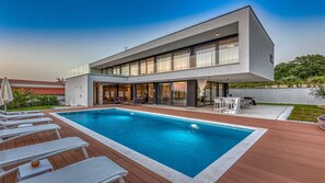 Une maison moderne à deux étages dotée d’une piscine, d’un espace salon extérieur et d’un patio.