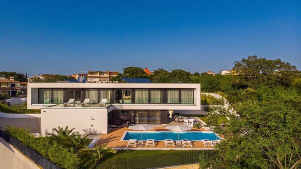 Une maison moderne à deux étages, dotée d’une terrasse sur le toit, d’une piscine et d’un jardin luxuriant.