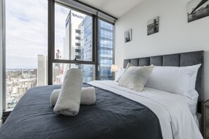 A modern hotel room with a large bed, a view of the cityscape, and a city skyline visible through the window.