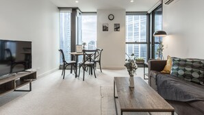 A modern living room with a flat-screen TV, a sofa, a coffee table, and a dining area with chairs and a table. - Trendy Melbourne 2 Bedroom Apartment by BnB Pro (Melbourne)